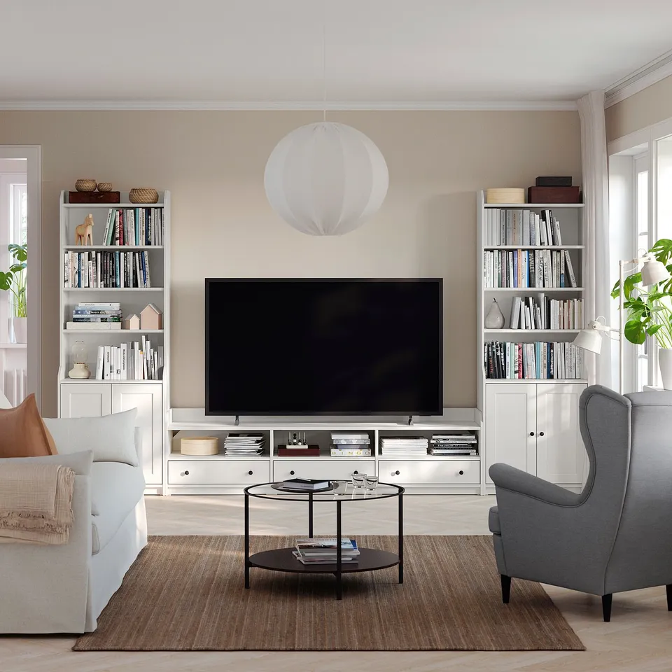 Modern living room with HAUGA tv unit, grey chair, white sofa, bookshelves, and decorations.