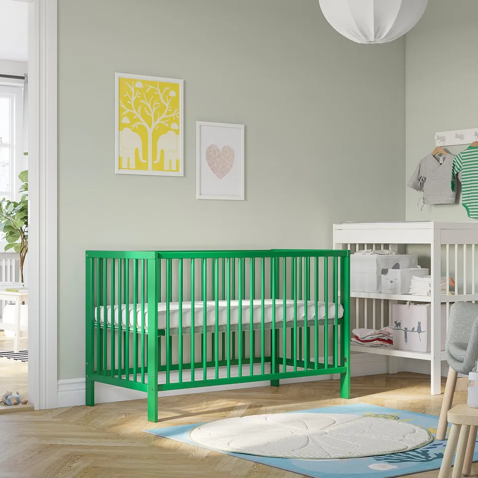 Green baby cot in nursery with removable side & sturdy wood.