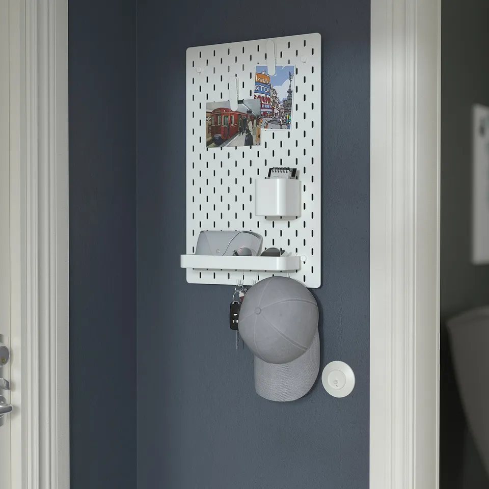 A wall-mounted SKÅDIS pegboard organises items like keys, wallet, and hat. It includes a cup holder and storage shelf.