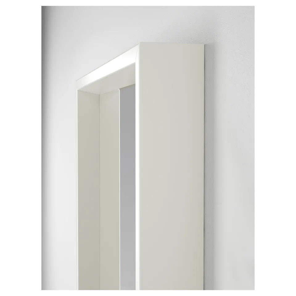 Modern, sleek, rectangular mirror with a clean white frame mounted vertically against a smooth grey wall, reflecting light brightly.
