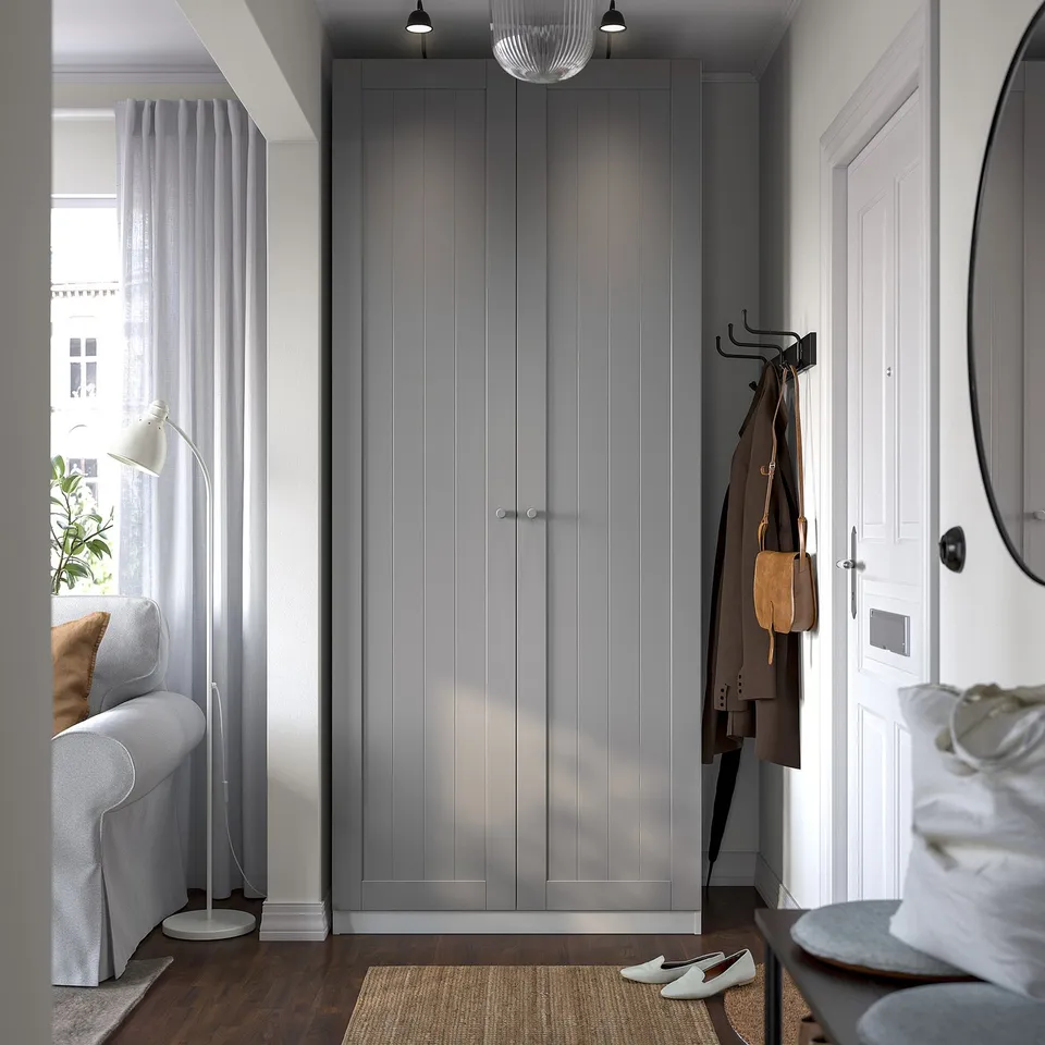 Modern entryway with IKEA PAX wardrobe, coat hooks, grey sofa, and floor lamp.