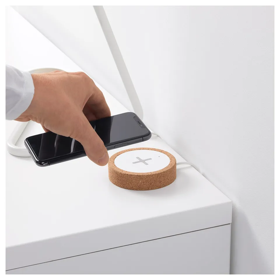 Person placing smartphone on cork wireless charger on white surface.