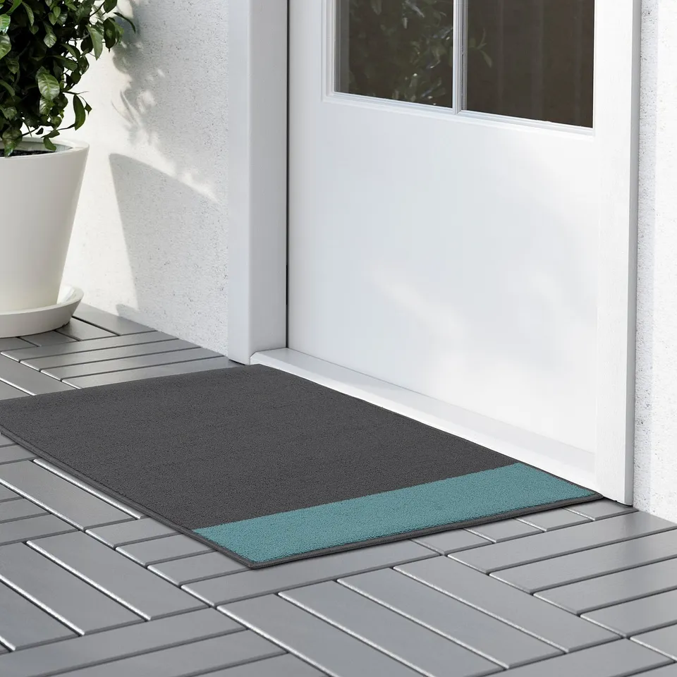 Modern doormat with grey and teal stripes sits outside a white door, featuring a non-slip backing for stability.
