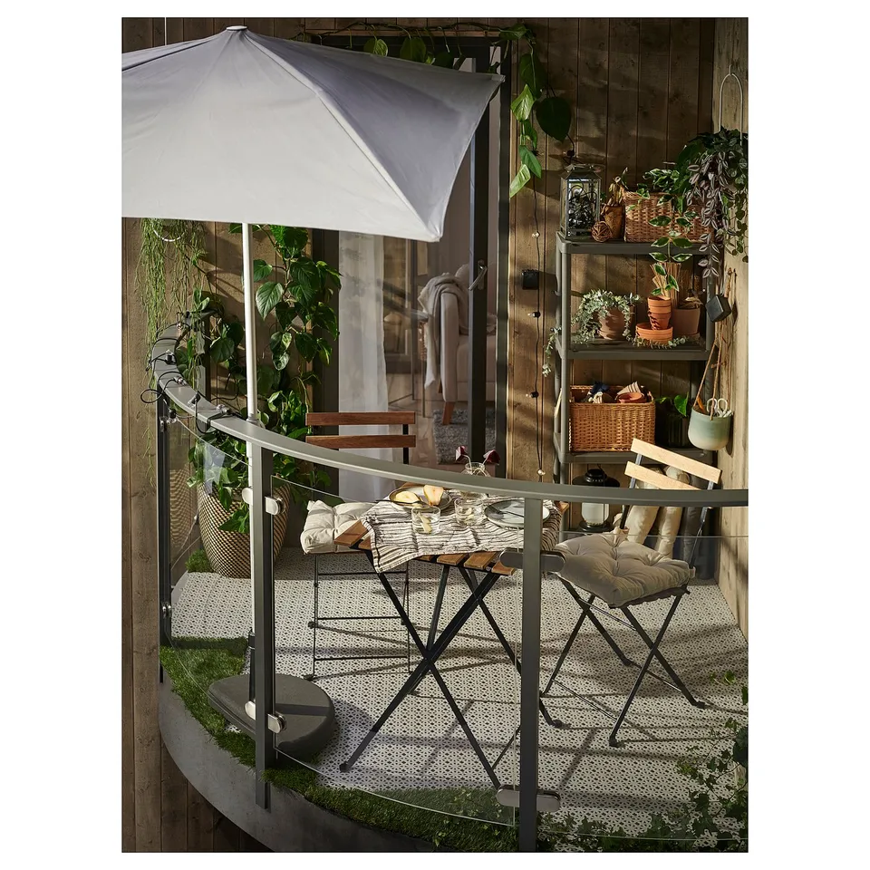 Small balcony with folding table and chairs, white umbrella, plants, and decor.