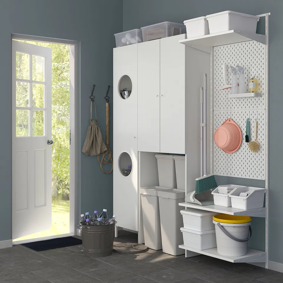 White laundry room organiser, NYSJÖN, above washer, with doors, shelves, and hooks, storing cleaning supplies.