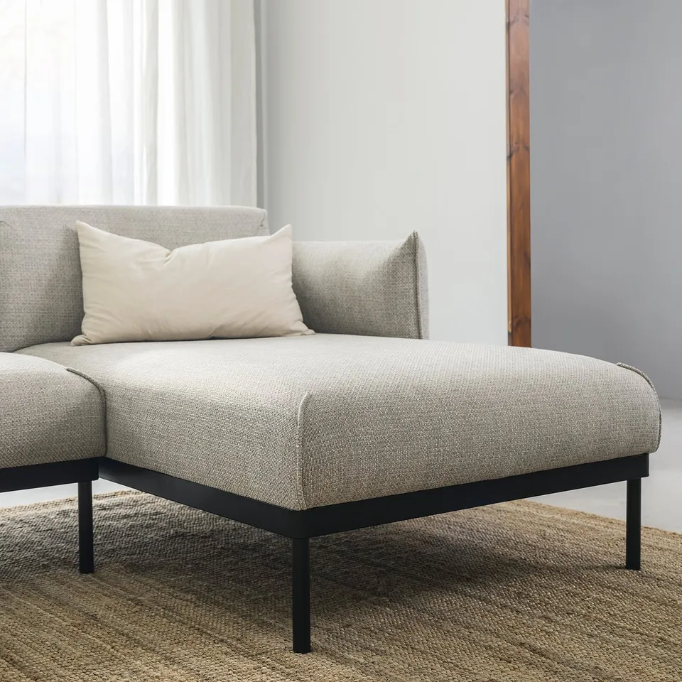 Modern grey sofa with clean lines, white pillow, black metal legs on striped rug.