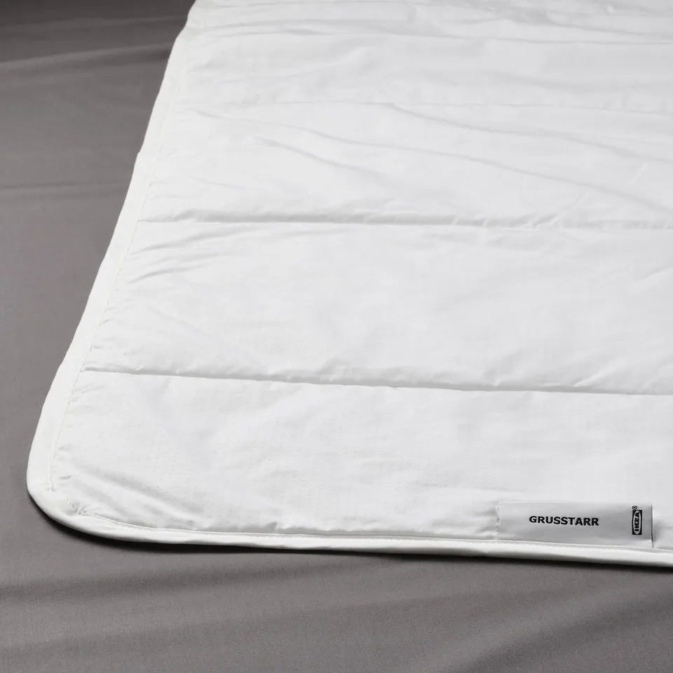 White duvet on grey bedding, smooth fabric, quality label visible at bottom.