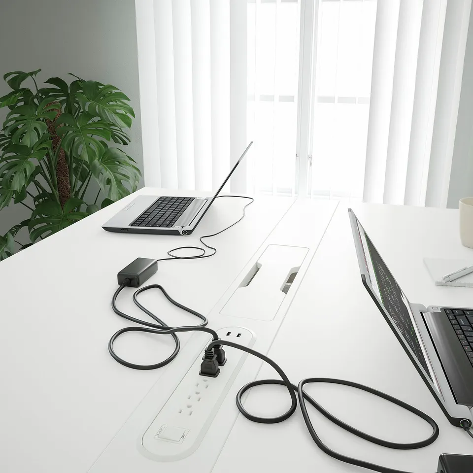 Modern office conference table with laptop chargers and cable management, suitable for sitting and standing.
