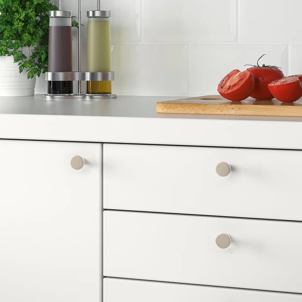 Modern kitchen setup with BAGGANÄS white knobs on drawers, stainless steel containers, and sliced tomatoes on a cutting board.