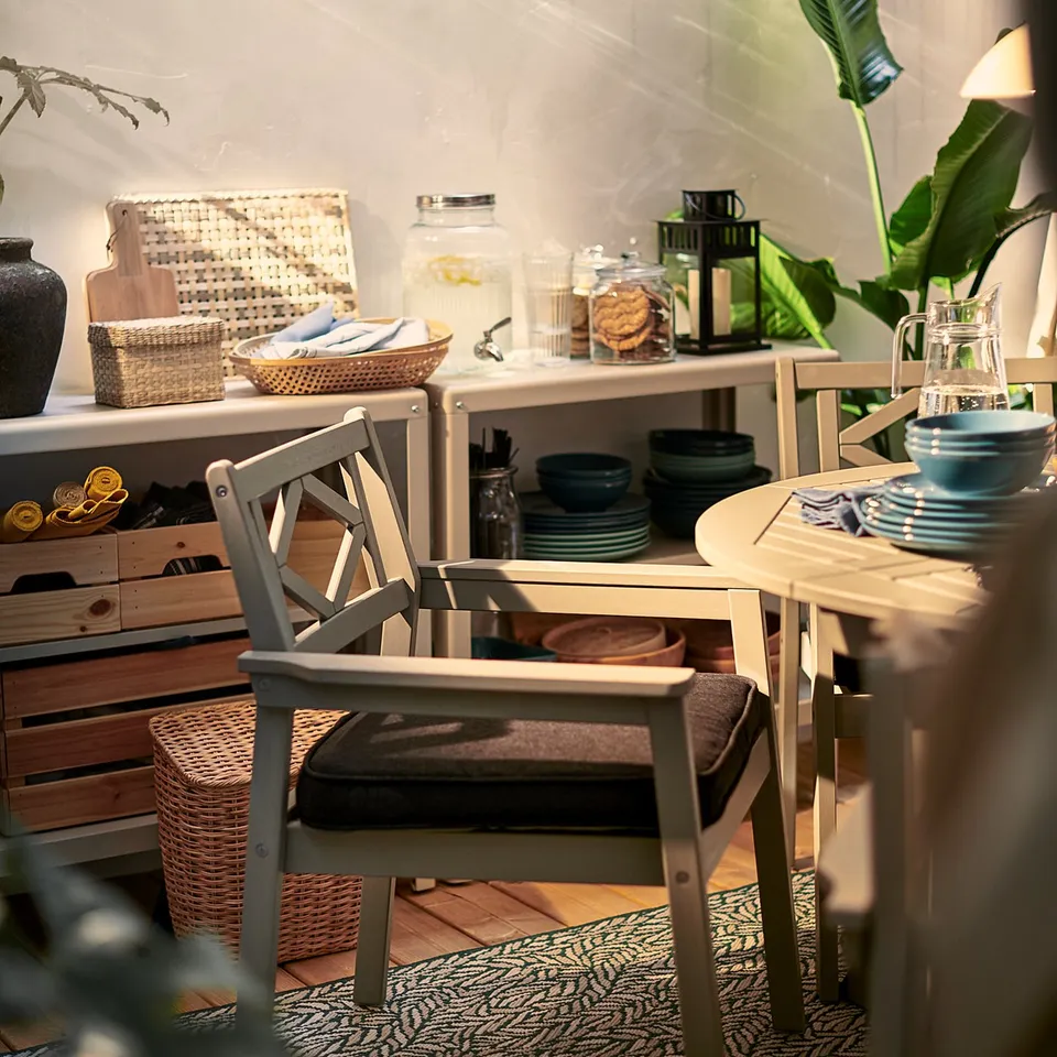 Outdoor seating with JÄRPÖN/DUVHOLMEN cushions, plants, dishes, and lanterns. String lights overhead.