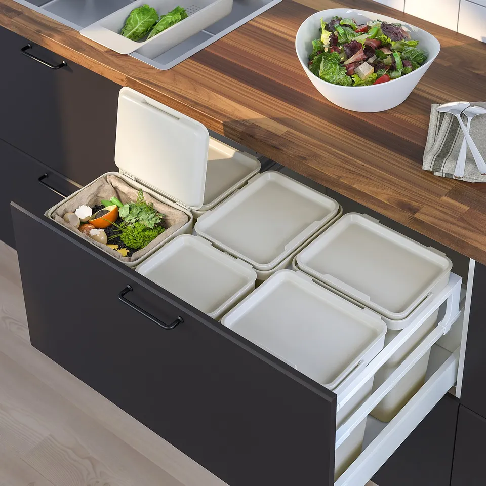 Modern kitchen setup with HÅLLBAR waste sorting in black drawer, wooden counter, and a salad bowl.