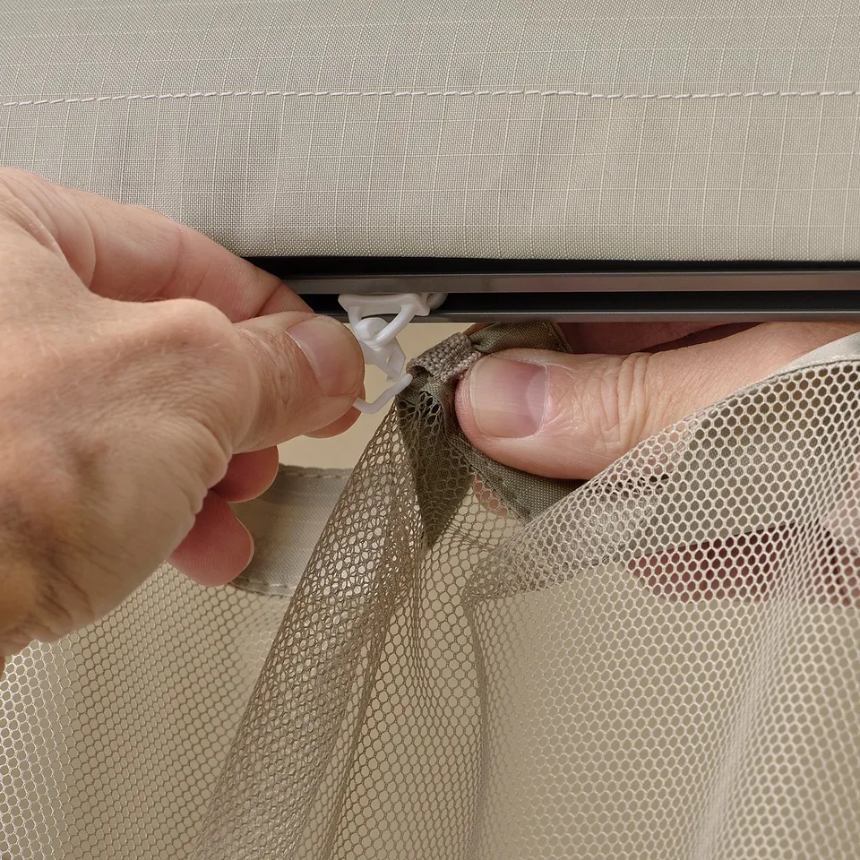 Hand attaches mesh net to gazebo frame using plastic clips.