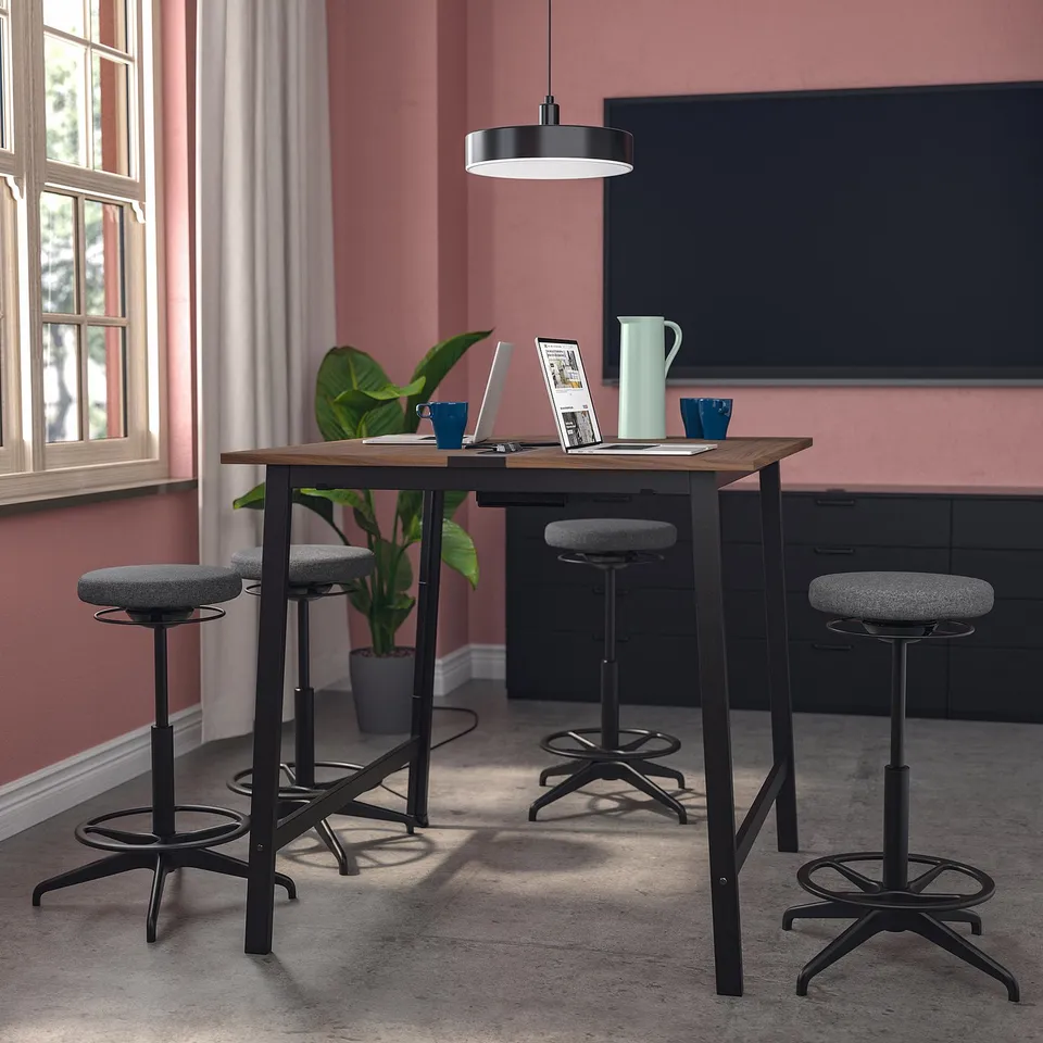 MITTZON conference table with high stools, wooden top, black metal base. Red walls, white curtains, large tv. Comfortable for meetings, modern design.