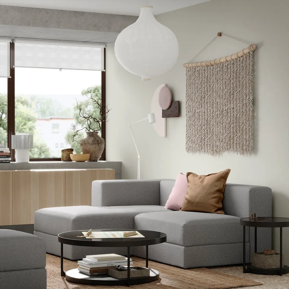 Modern living room with grey JÄTTEBO modular sofa, pillows, coffee table, large window, wall hanging, and pendant lamp.