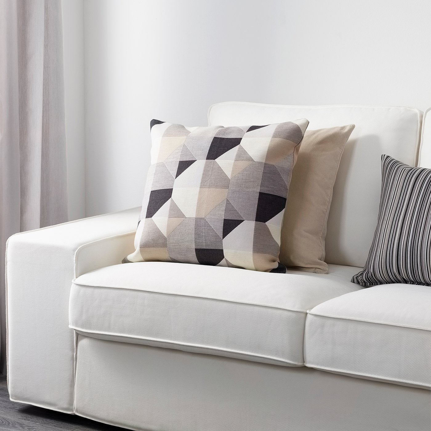 Modern white sofa with oversized, geometric-patterned square pillows in neutral tones.