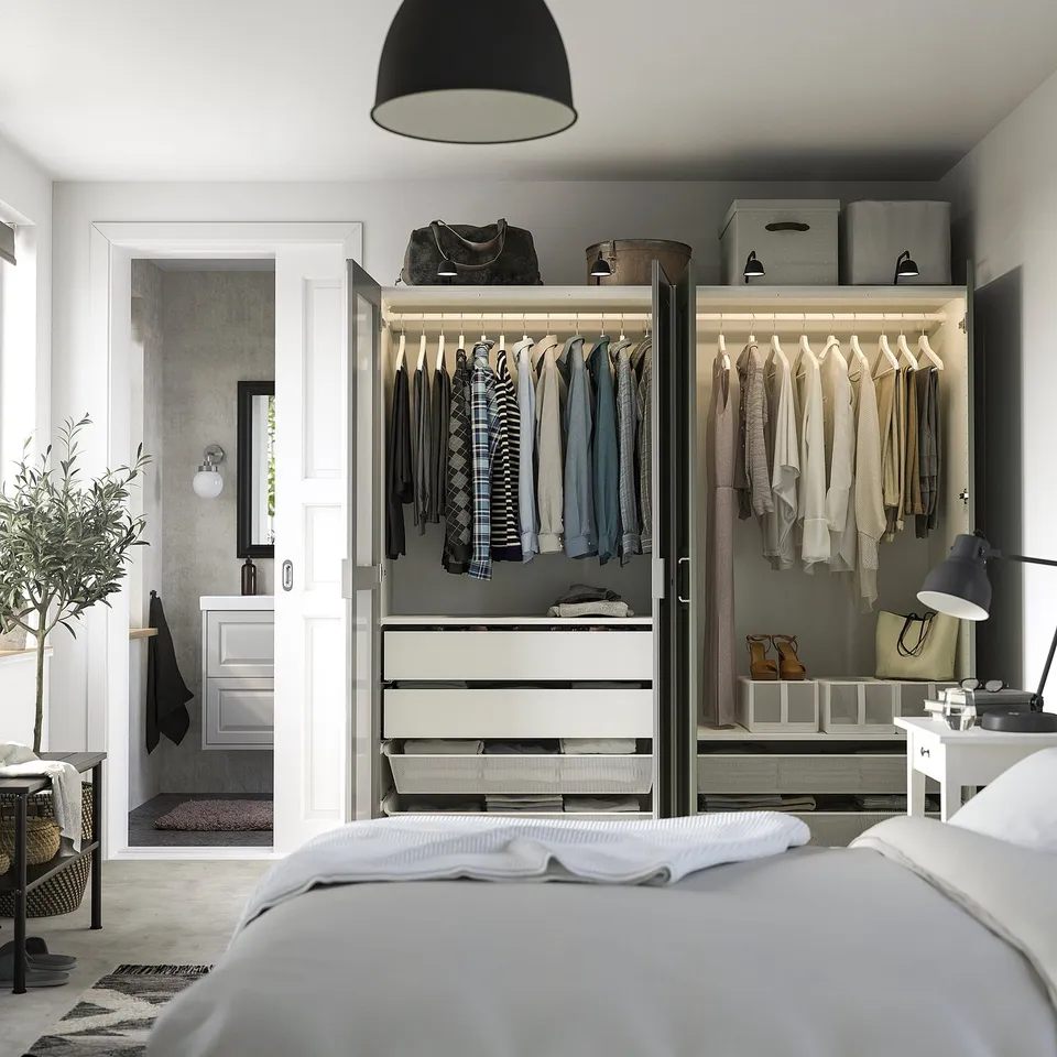 Bedroom with open wardrobe showing clothes, drawers, and organisers. Mirrored door reflects light, creating a larger space feel.