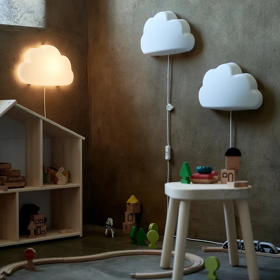 Kids corner with white cloud lamps, wooden toys, and bookshelf. Soft light, playful design.