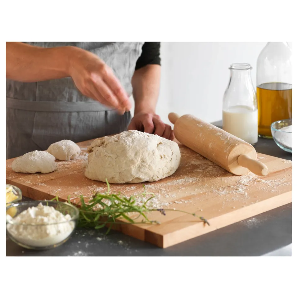 A person making dough, wooden rolling pin on floured board, bowls of ingredients.