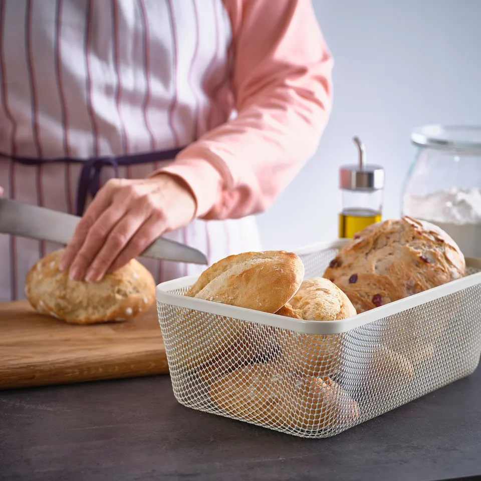 A person reaches into a mesh IKEA 365+ storage basket holding bread, promoting air circulation and room temperature storage.