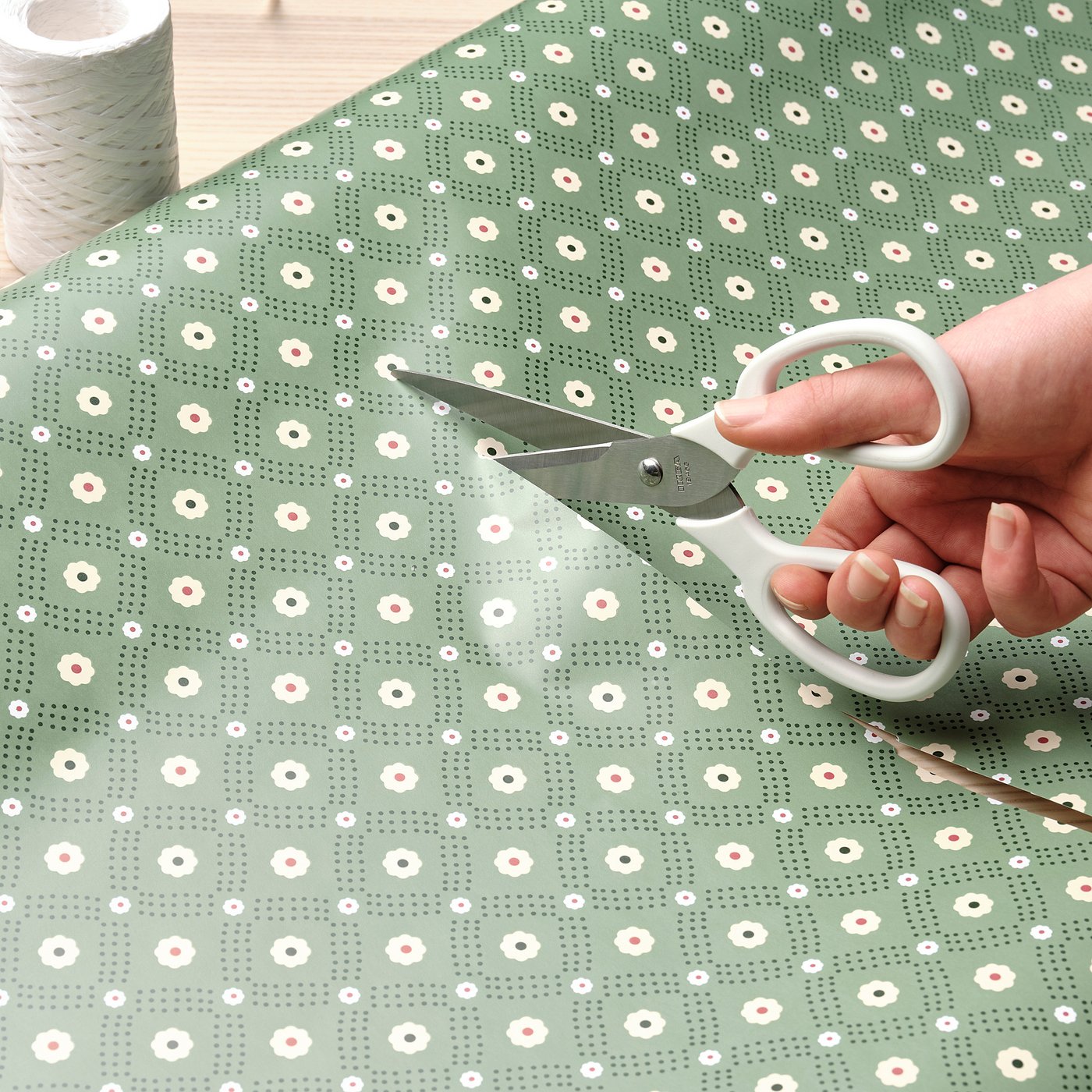 Person cutting green patterned paper with floral scissors.
