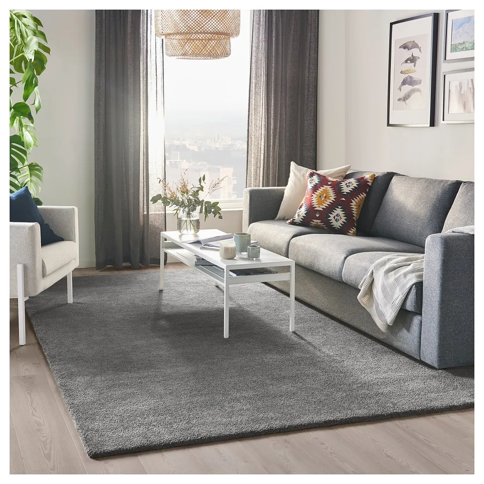 Modern living room with grey STOENSE rug, sofa, pillows, coffee table, city view.