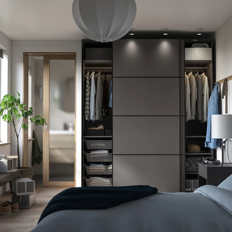 Modern bedroom with grey PAX wardrobe; sliding doors, hanging clothes, adjustable shelves, and integrated lighting.