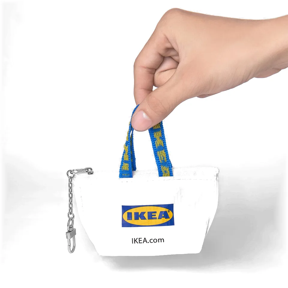 Hand holds a white tiny IKEA bag with a blue yellow rope handle and zip, attached by a carabiner.