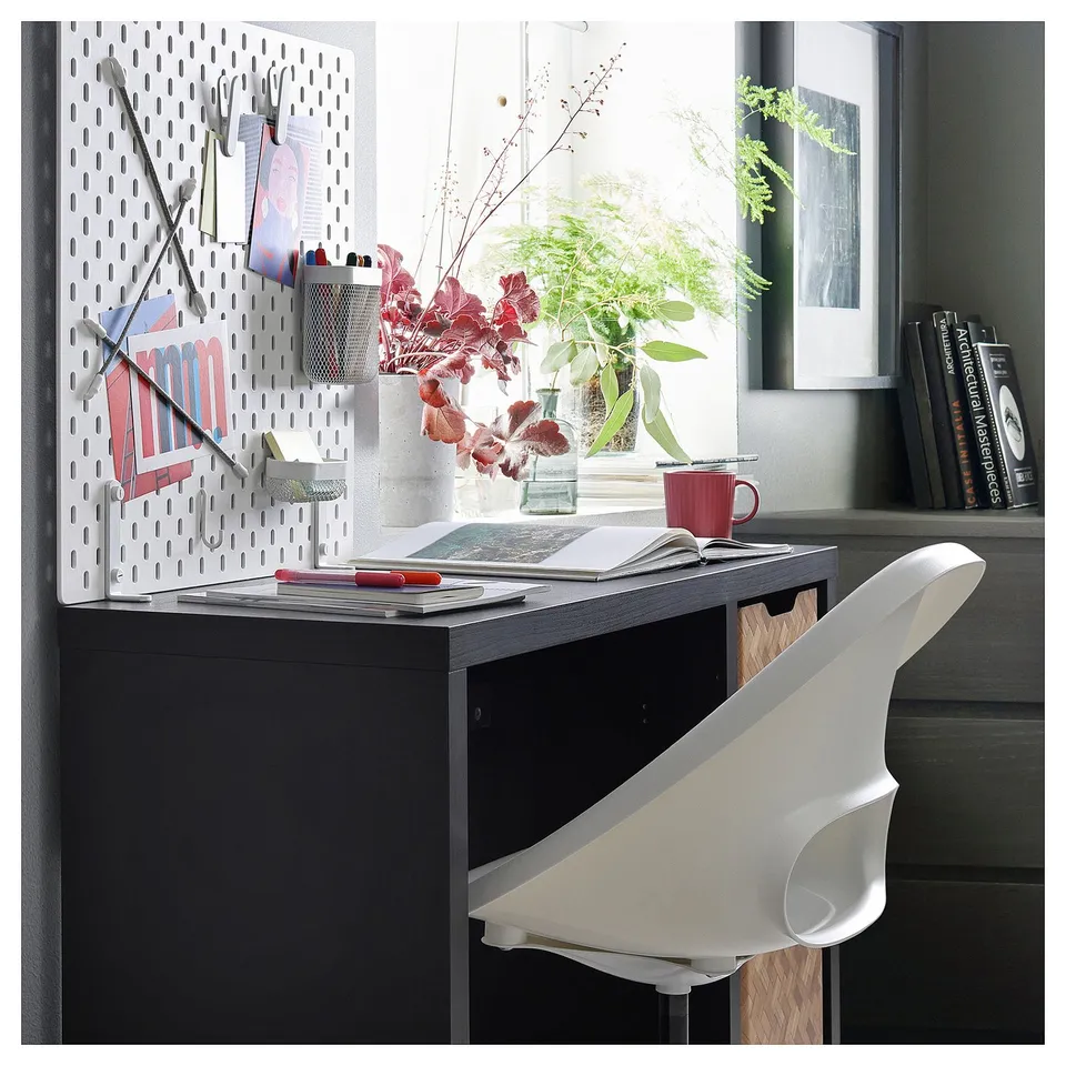 Black KALLAX desk with pegboard, chair, plants, books. Minimalist home office setup.
