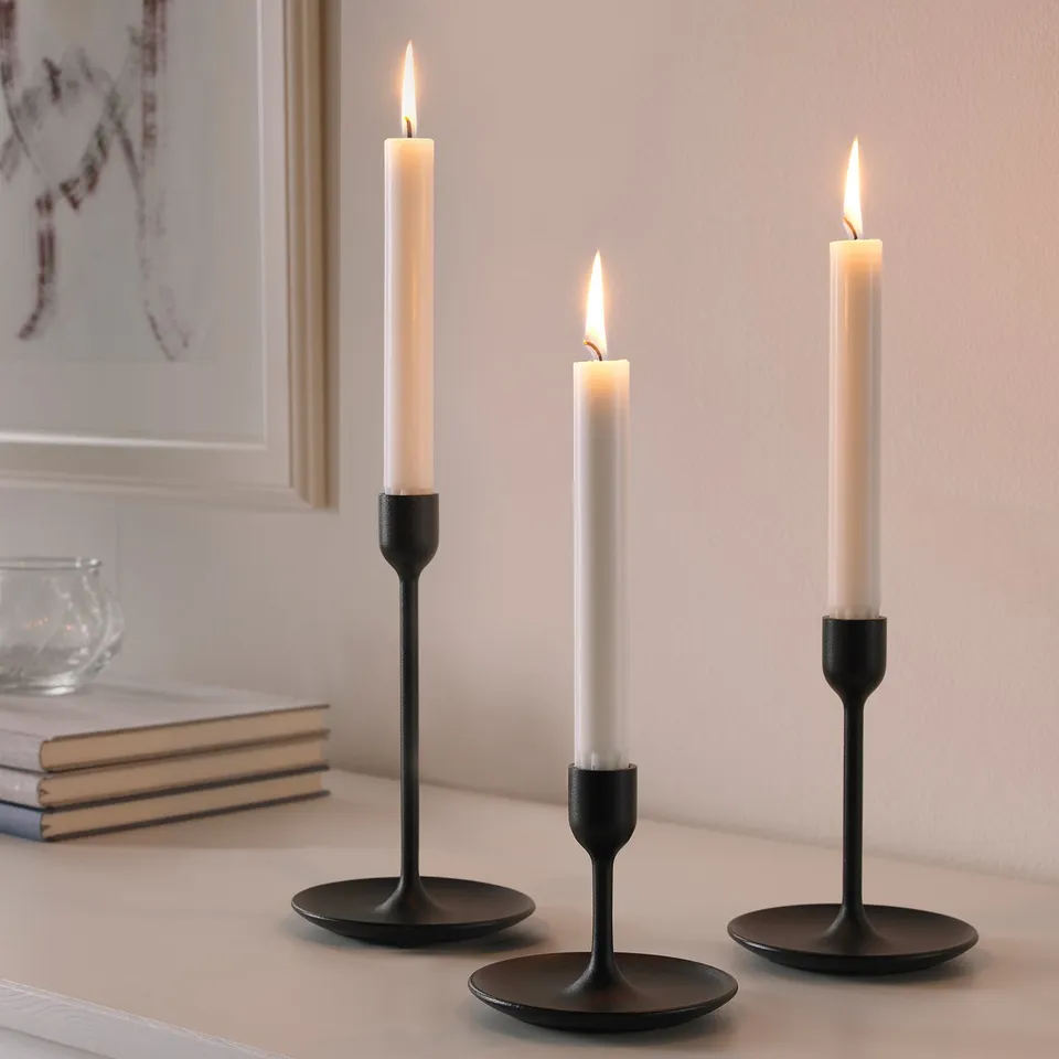 Three black candlesticks of varying heights with lit candles on a table, creating a warm and cosy atmosphere. Part of the FULLTALIG set.
