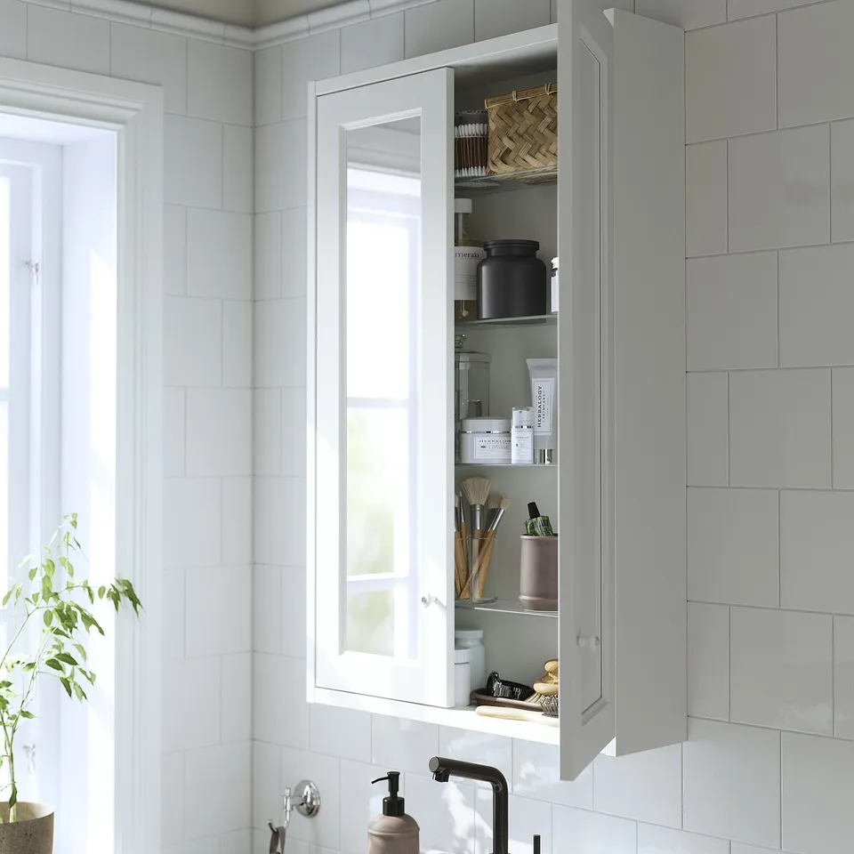 A white bathroom cabinet with mirrored doors, reflecting organised items, mounted above a sink.