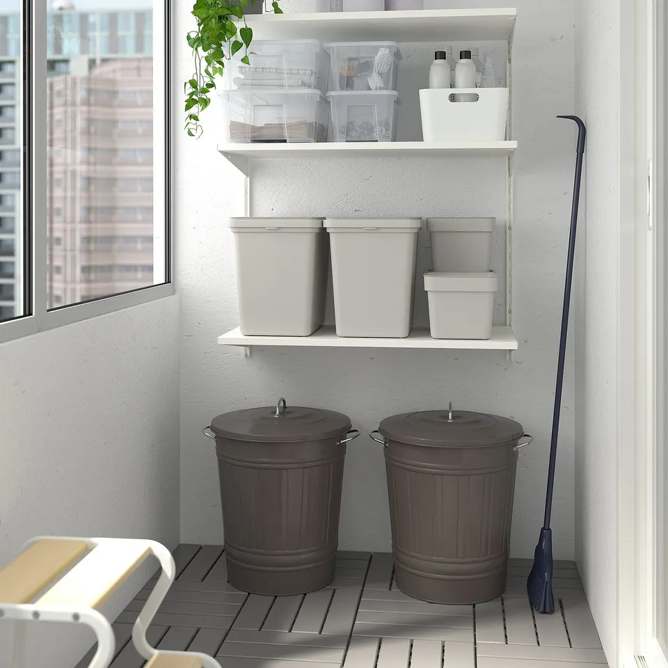 Two large grey KNODD bins with handles and lids on tiled floor, below a white shelf, near a window for substantial storage.