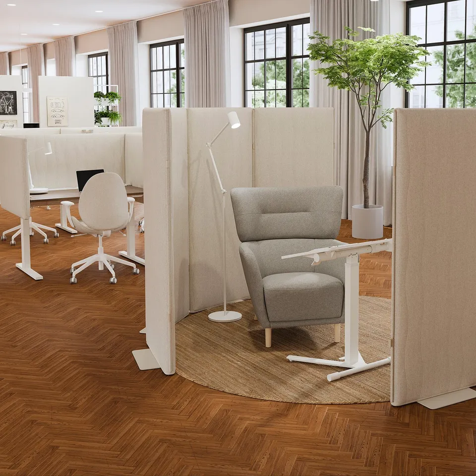 Modern office with MITTZON beige acoustic screens, armchair, lamp, hardwood floor & large windows. Screens taller than chair for privacy.