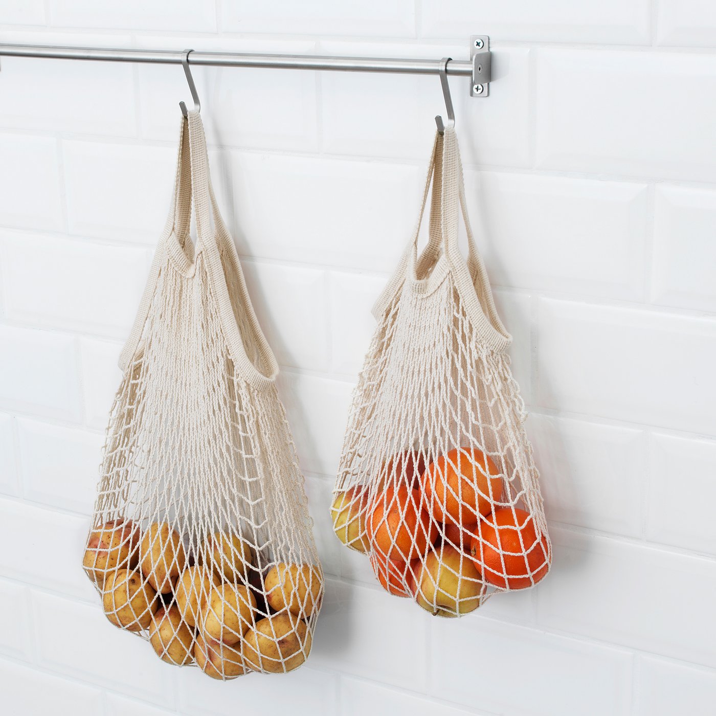 Two KUNGSFORS net bags hang from hooks, each filled with fruits and vegetables. The bags keep produce fresh by allowing air circulation.