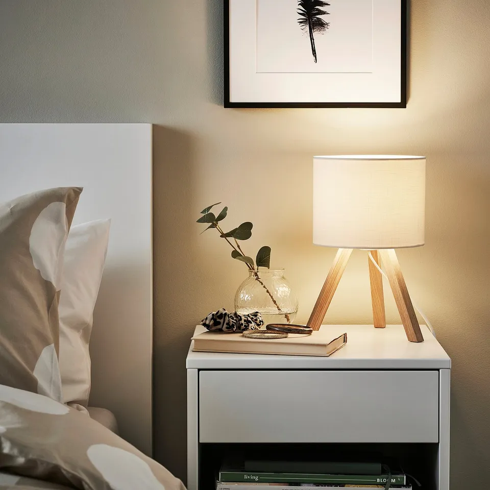 Bedside table with STORSEGEL lamp, books, and flowers.
