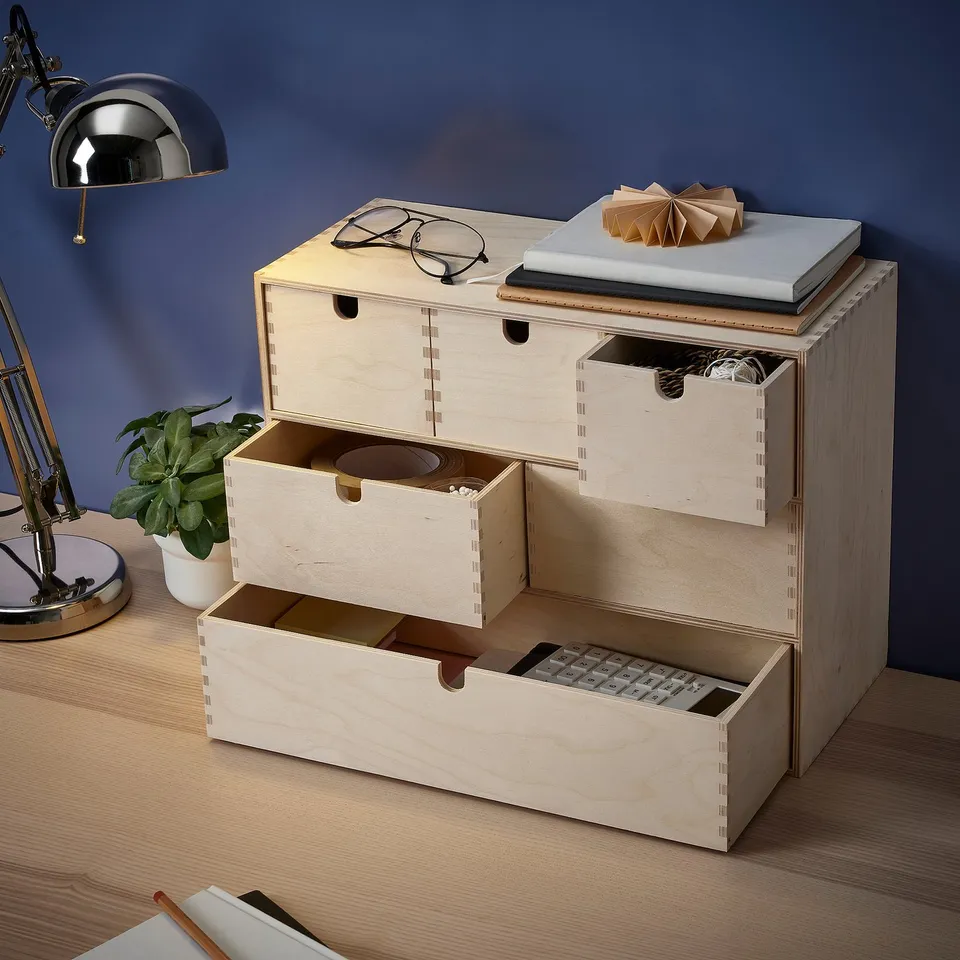 Wooden desk organiser with multiple drawers on a table, a lamp, and a plant.
