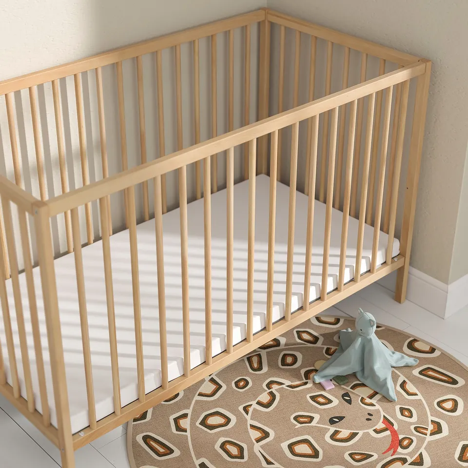 Baby crib with thin mattress, light wood, round rug, blue toy. Mattress fits perfectly.