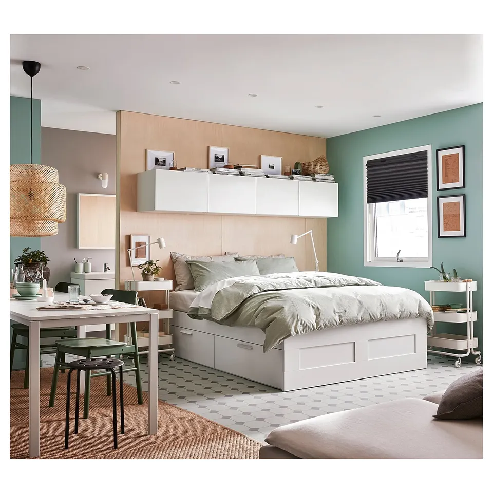 Modern bedroom with white BRIMNES bed, green walls, and built-in shelves. Adjustable bed, storage drawers, and green chairs around a dining table.