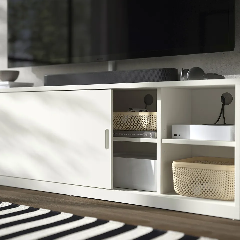 Modern white tv stand with open and closed storage, organised with woven baskets and electronics, sleek design.