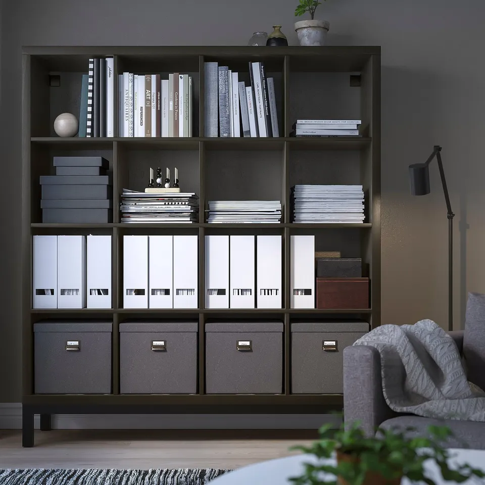 KALLAX black shelving unit with multiple storage sections, holding books and files, beside a grey sofa.