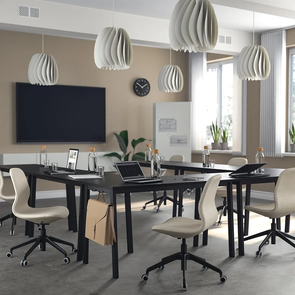 Modern conference room with black MITTZON tables and beige långfjäll chairs. Tables hold laptops, glasses, and bottles.