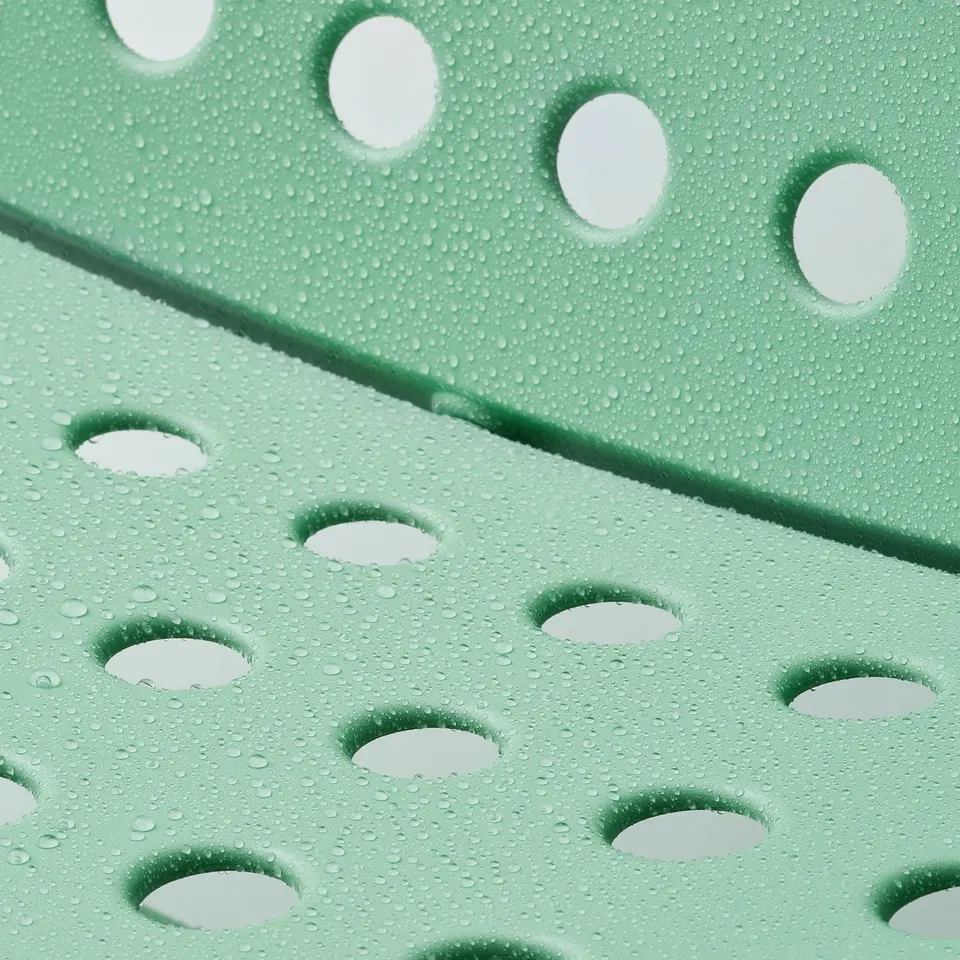 Perforated green outdoor chair with water droplets, designed for comfort and easy cleaning.