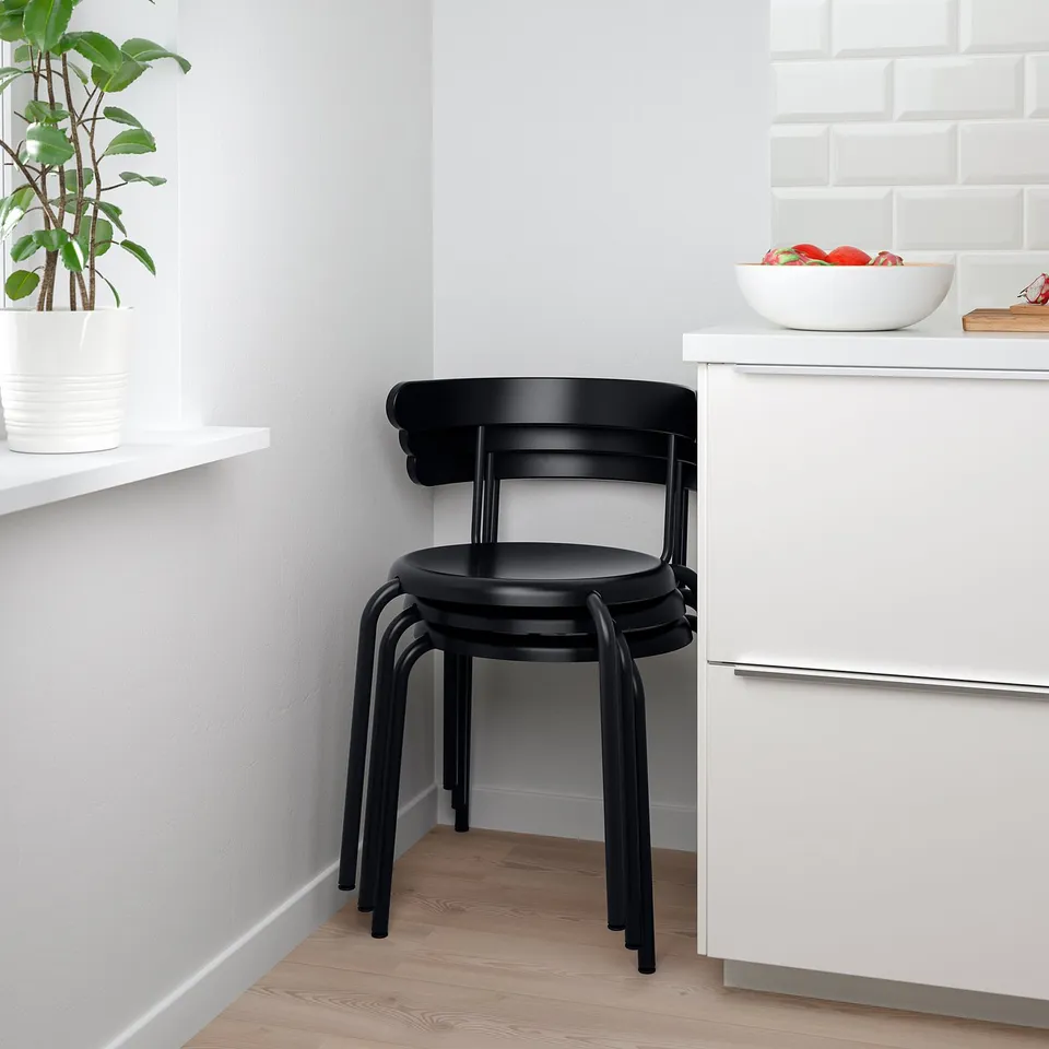 Stacked black chairs near white cabinet with bowl of fruit. Ideal for space-saving.