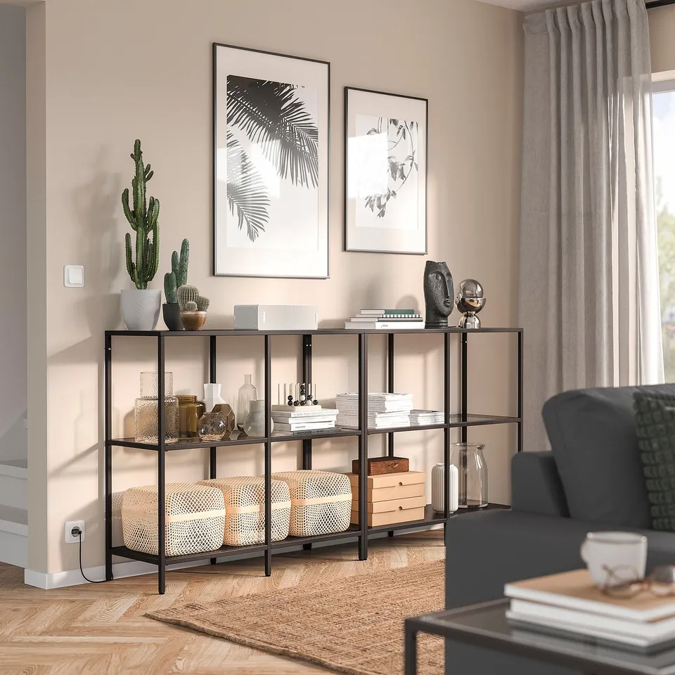 Modern living room with VITTSJÖ shelf, plants, vases, books, dark green armchair, art, and coffee table.