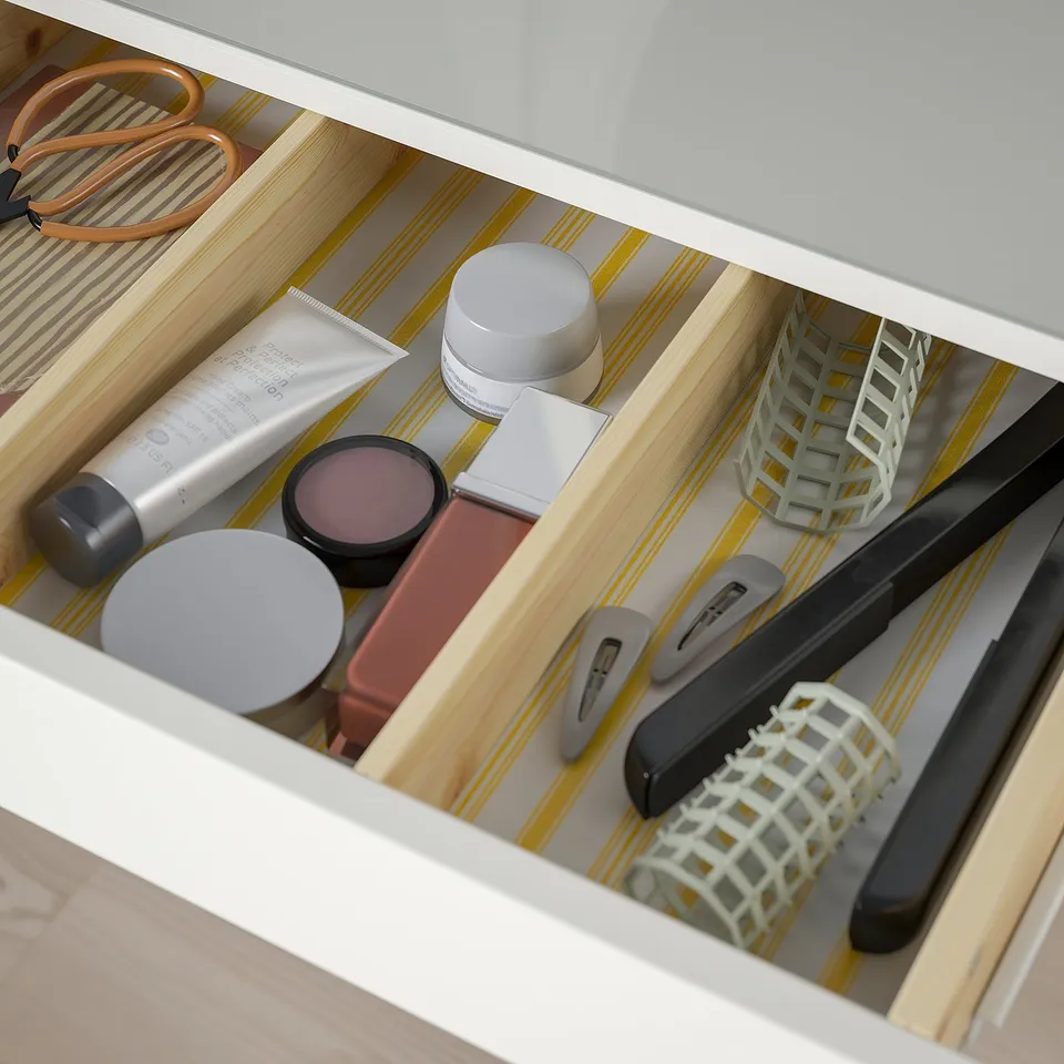 Open drawer of white HEMNES dresser holding makeup, brushes, and hair tools.