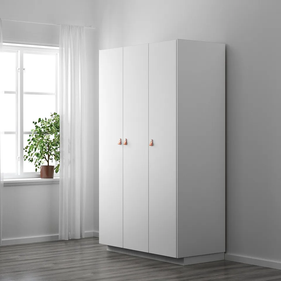 White wardrobe with leather handles beside a window with a plant.