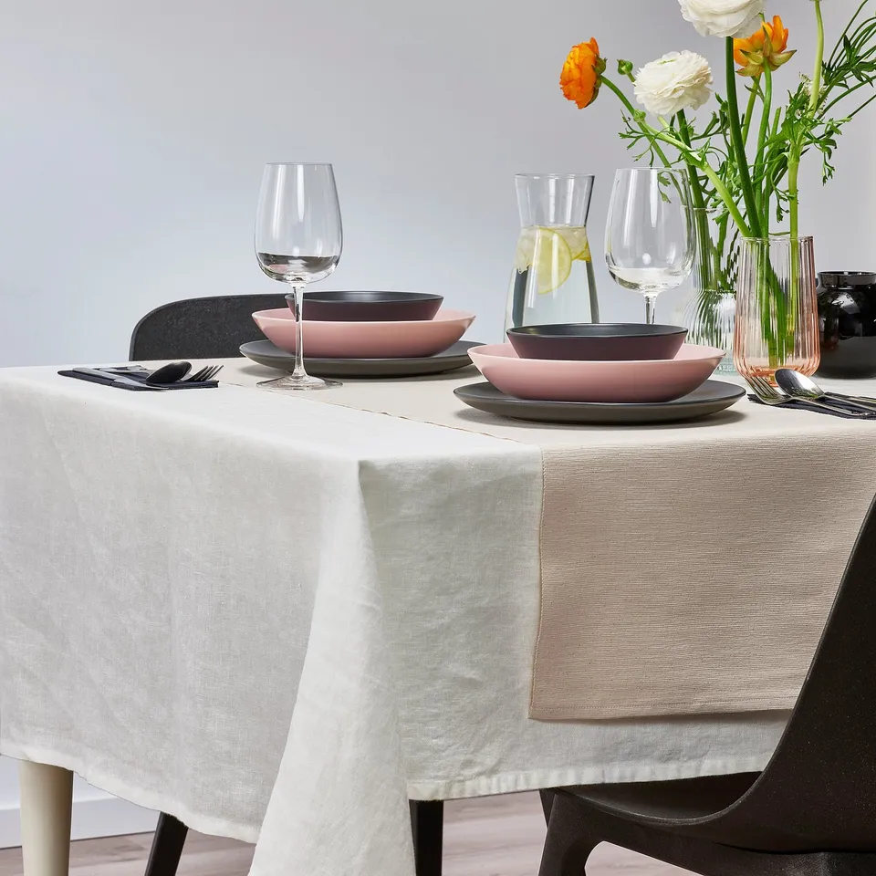 Table set for two with modern dishes, glasses, and vase holding colourful flowers on a white tablecloth.