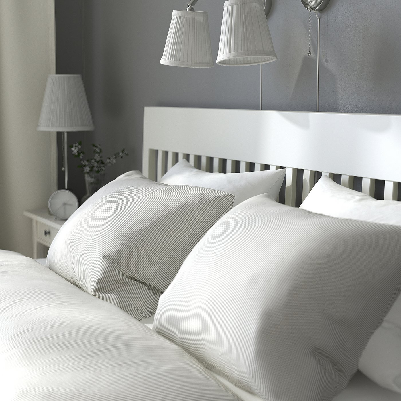 Serene bedroom: IDANÄS white bed with striped pillows. Two lamps and clock on bedside table.