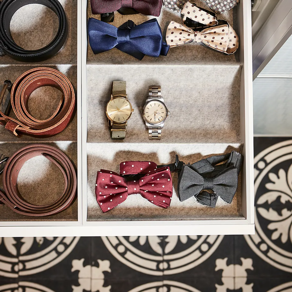Organised drawer with belts, watches, and bow ties in compartments, top sweater.