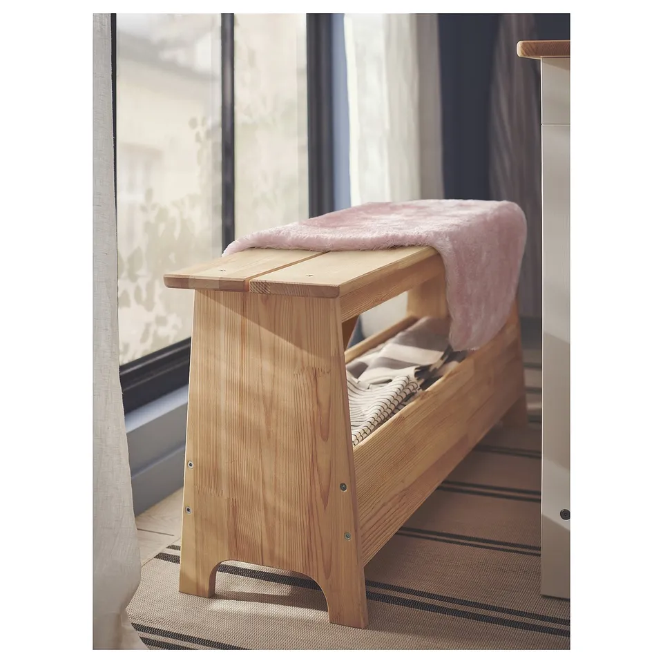 Light wood bench with soft pink blanket, near window.