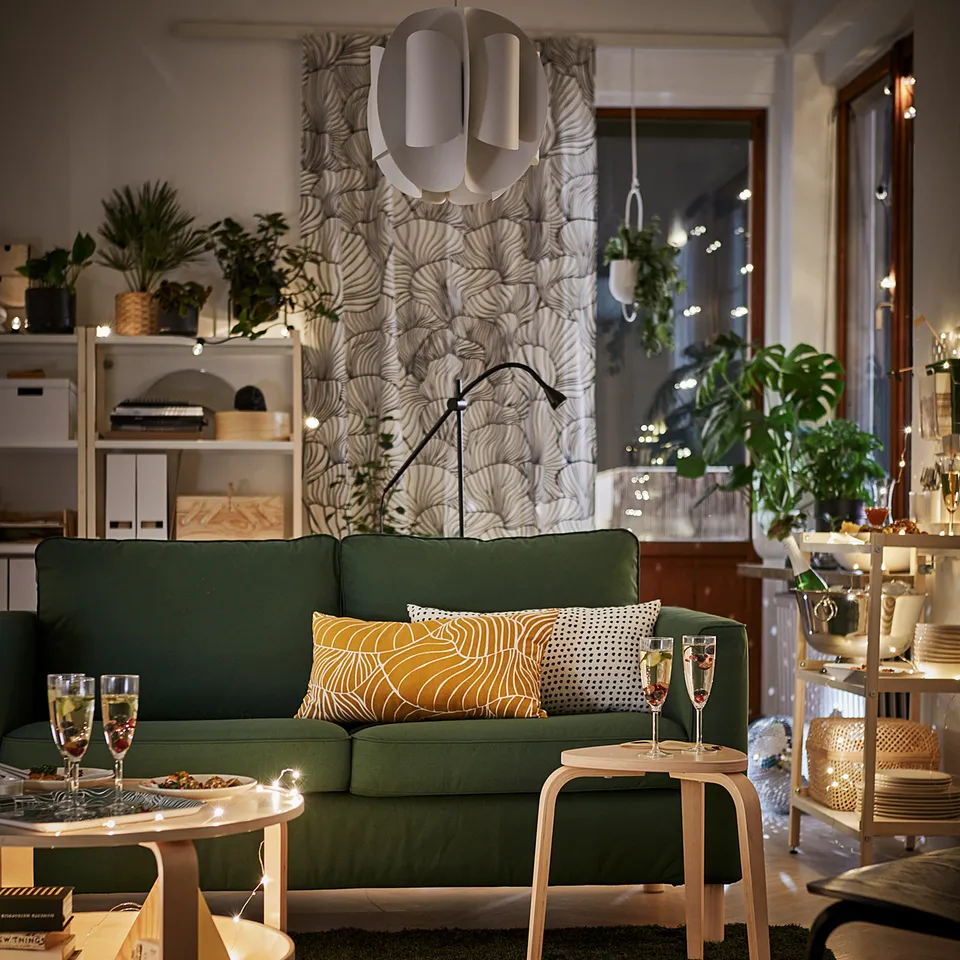 Modern living room with green KYRRE stools, decorative lights, plants, and a green sofa with unique pillows.
